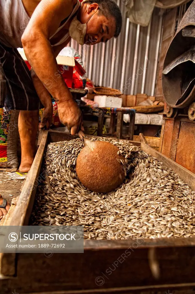 a man scoops seeds from a wooden crate, ruili yunnan china