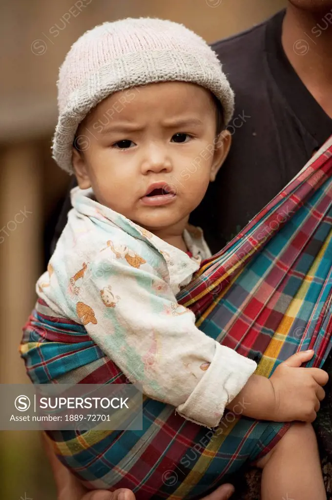 a young karen refugee child being carried in a sling, noh poh mae sot chiang mai thailand