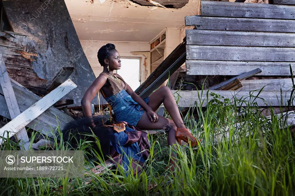 a young woman sits at the back of a dilapidated house, leduc, alberta, canada