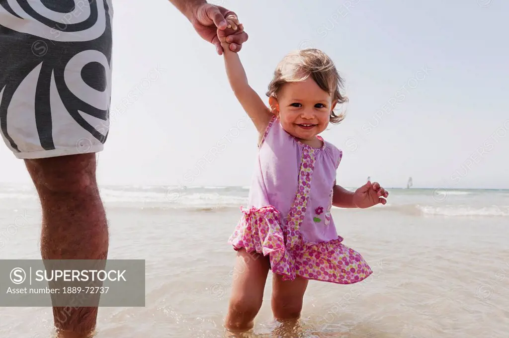 a young girl standing in the ocean holding her father´s hand, tarifa cadiz andalusia spain