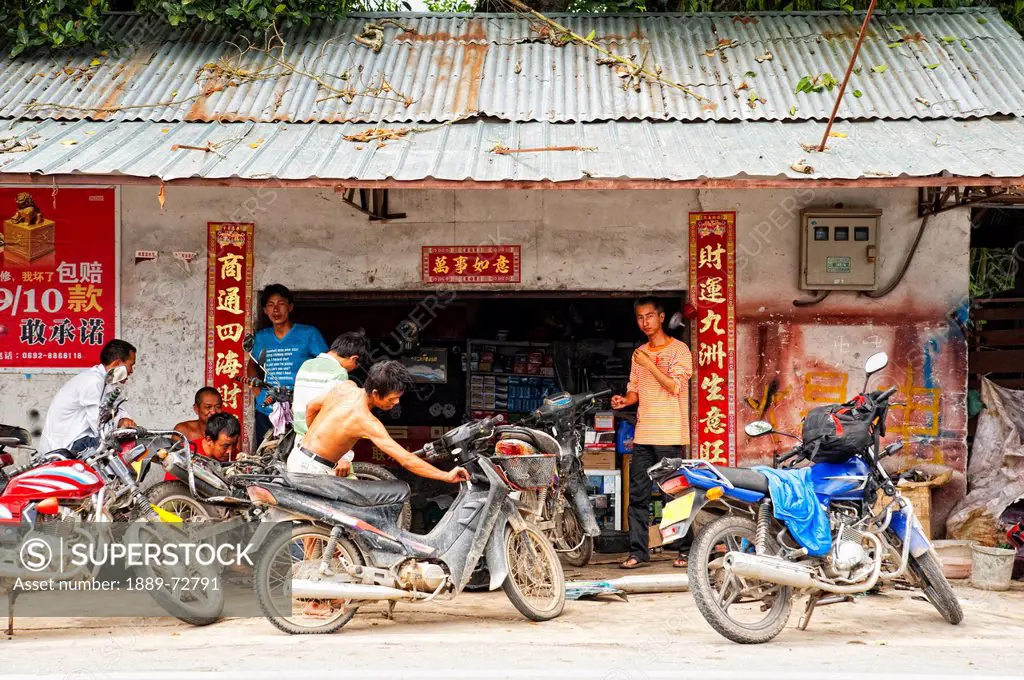 young men gather outside a building with their parked motorcycles, ruili yunnan china
