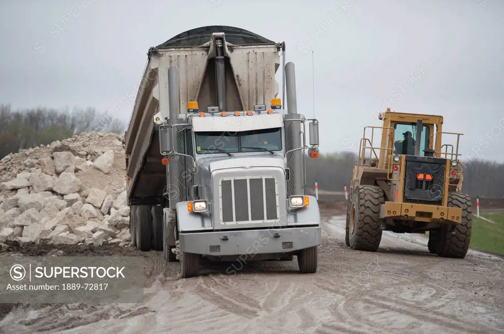 truck and tractor move rock to make a barrier in a flooded area, newton manitoba canada