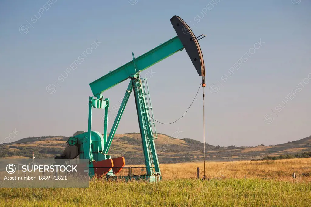 pumpjack in a field in the foothills at sunrise with blue sky, longview alberta canada