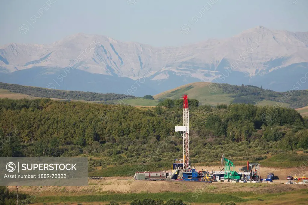 drilling rig with pumpjacks in the foothills with mountains in the distance and blue sky, longview alberta canada
