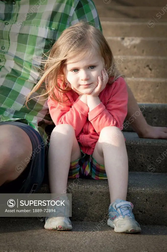 a young girl cradles her face in her hands as she sits on a step beside her father, bellingham washington united states of america