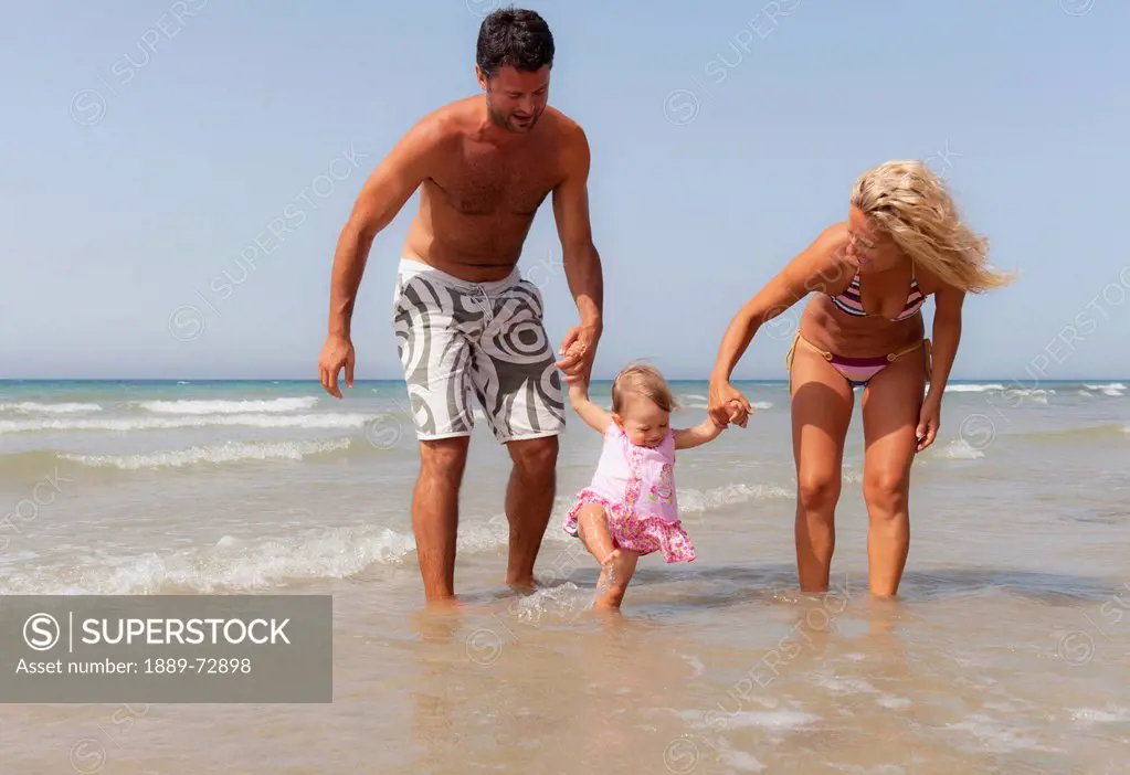 a mother and father playing with their young daughter on the beach, tarifa cadiz andalusia spain