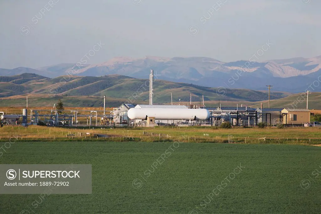small gas plant with white cylindrical tanks with foothills and mountains in the background at sunrise, longview alberta canada