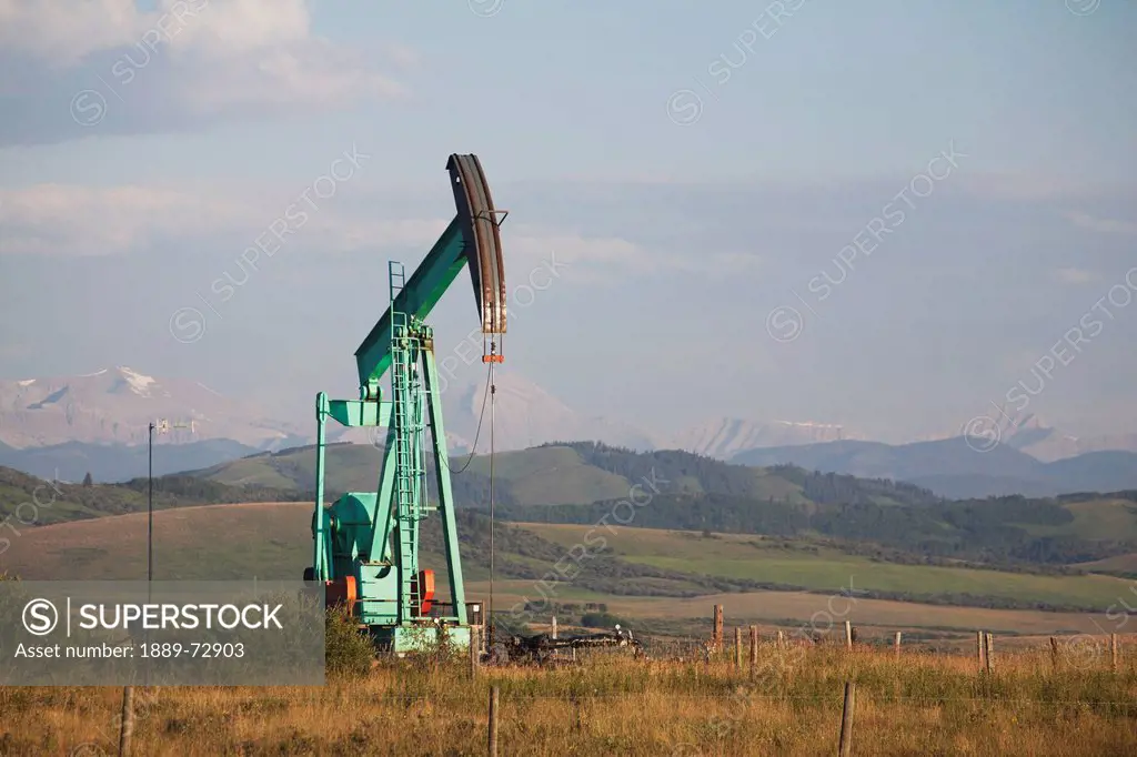 pumpjack in a field in the foothills with mountains in the distance at sunrise, longview alberta canada