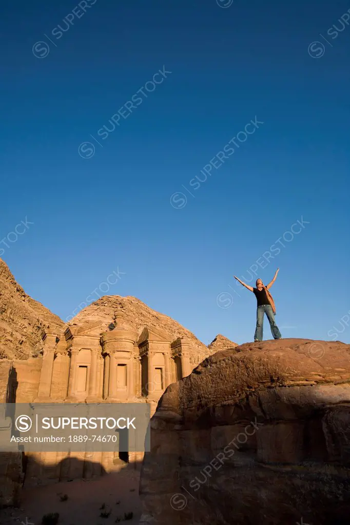A Woman Tourist Raises Her Arms In Front Of The Nabatean Ruins Of The Monastery, Petra Jordan