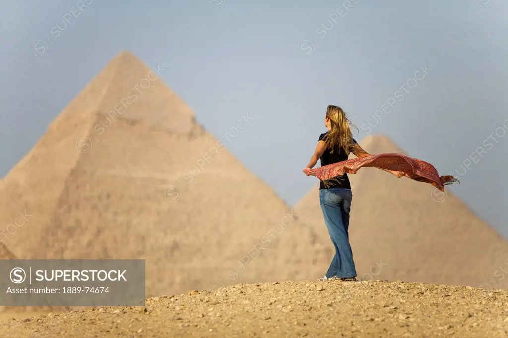 A Female Tourist Holds A Silk Scarf In The Wind As She Looks Out Toward The Pyramids Of Giza Near Cairo, Giza Egypt