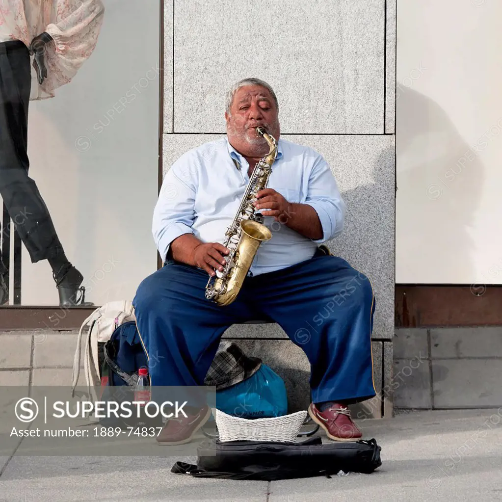 A Man Sits And Plays His Saxophone On The Sidewalk, Oslo Norway