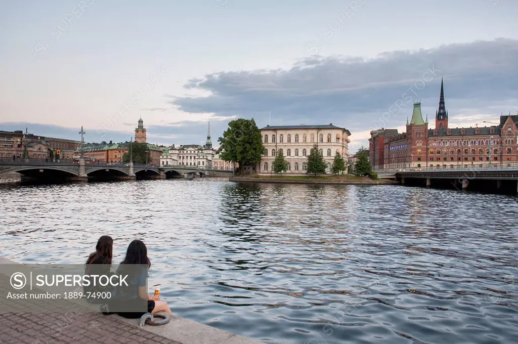 Two young women sitting together at the water´s edge, stockholm sweden