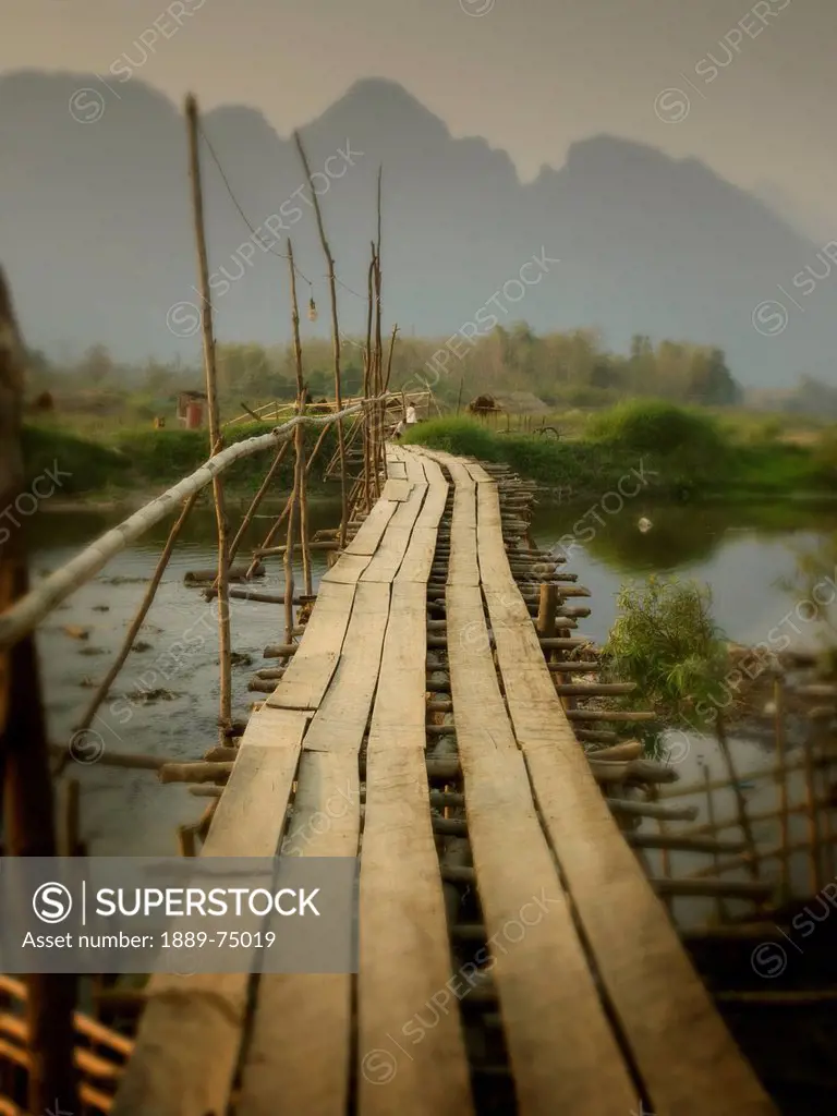 Wooden bridge over a river with mountains in the background, vang vieng laos