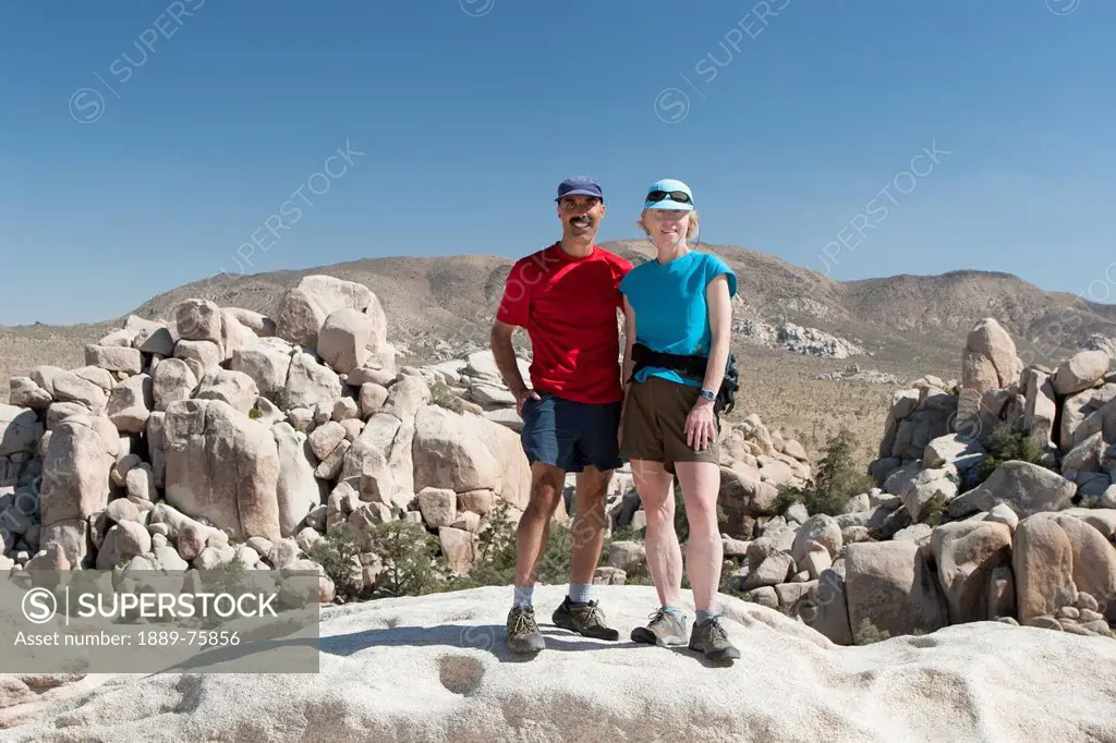 Male And Female Hikers On Top Of Rock With Rounded Rock Formations In The Background And Blue Sky, Palm Springs California United States Of America