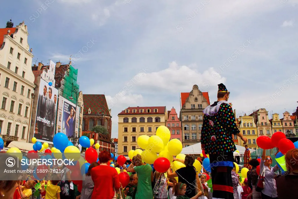 A clown on stilts amongst a crowd holding colourful balloons during a parade on rynek square or market square, wroclaw poland