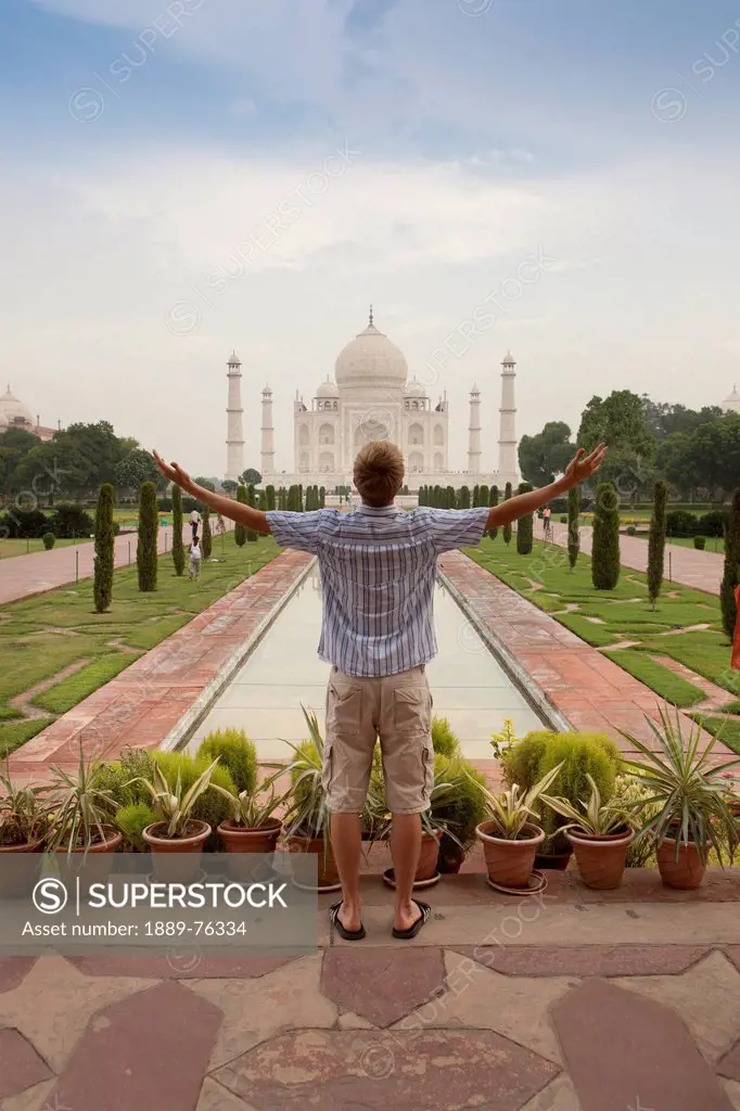 A young man with arms outstretched as he looks at the tah mahal, agra uttar pradesh india
