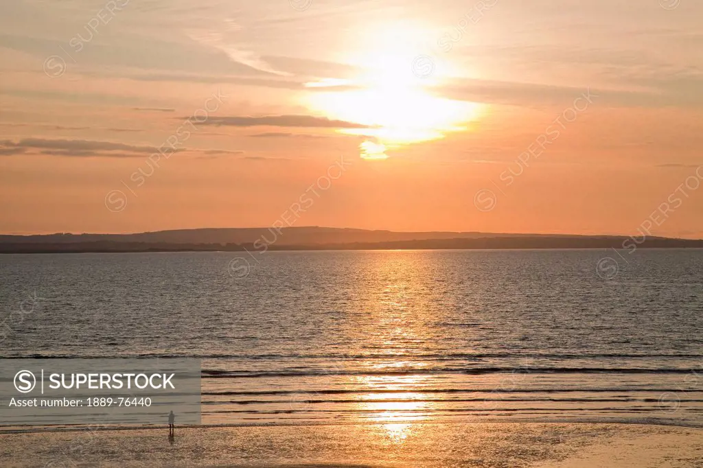 Silhouette of a person standing on the beach at the water´s edge at sunset, inishcrone county sligo ireland
