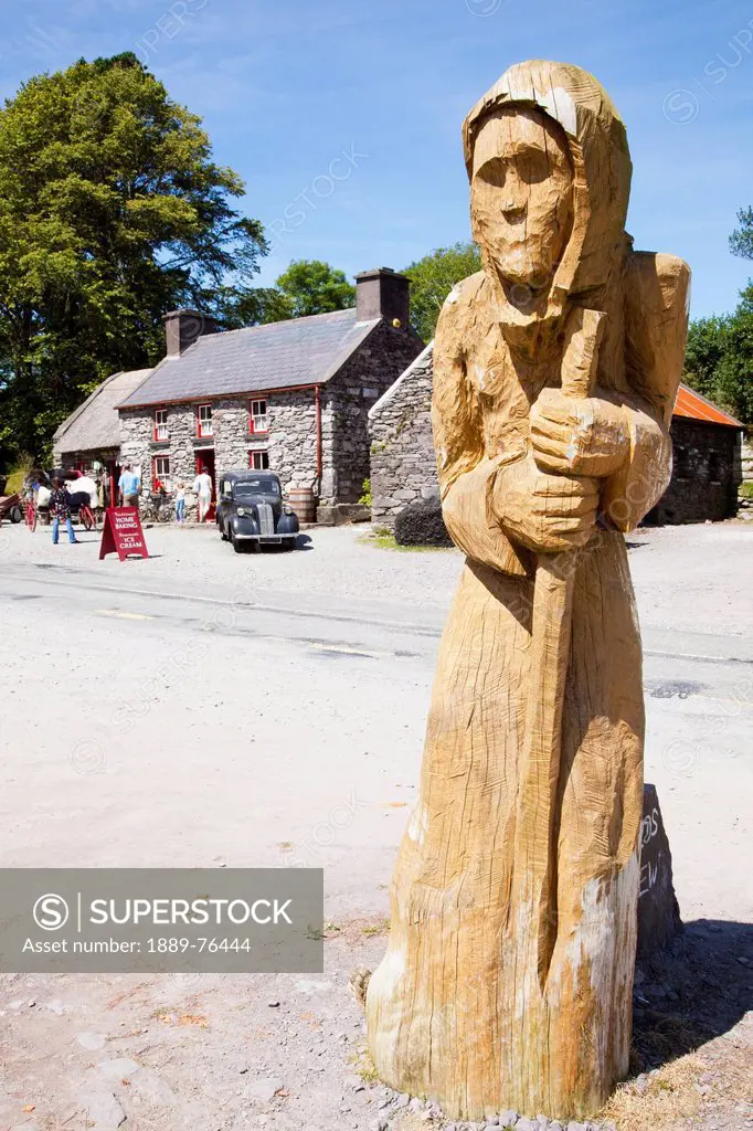 A carved wooden sculpture of a woman with molly darcy craft shop in the background, county kerry ireland
