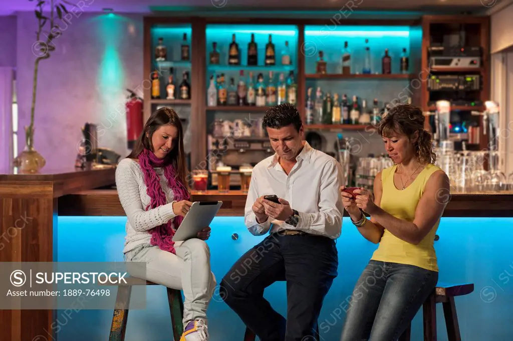 Three people sitting at the bar in republica cafe using their technology, tarifa cadiz andalusia spain