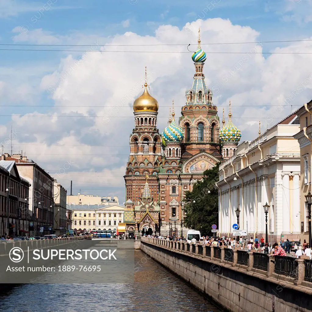 Pedestrians on the promenade along the griboedova canal with church of the savior on spilled blood in the distance, st. petersburg russia