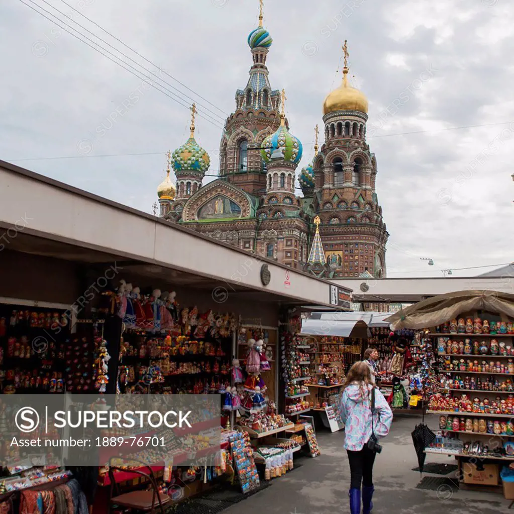A young woman walks through a market area with the church of the savior on spilled blood in the background, st. petersburg russia