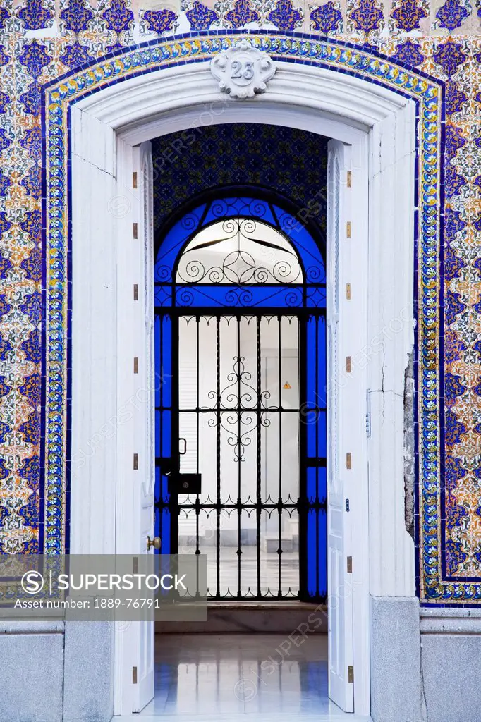 An open doorway on a building with ornate facade leading into a room with a gate surrounded by blue glass, chiclana de la frontera andalusia spain