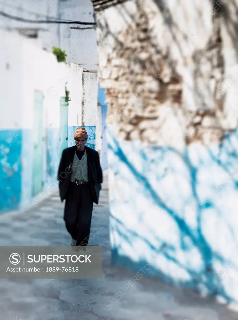 A man walking down an alleyway between buildings, asilah morocco