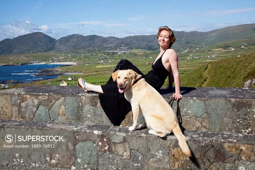 A woman and her dog sit on a stone wall near allihies, county cork ireland
