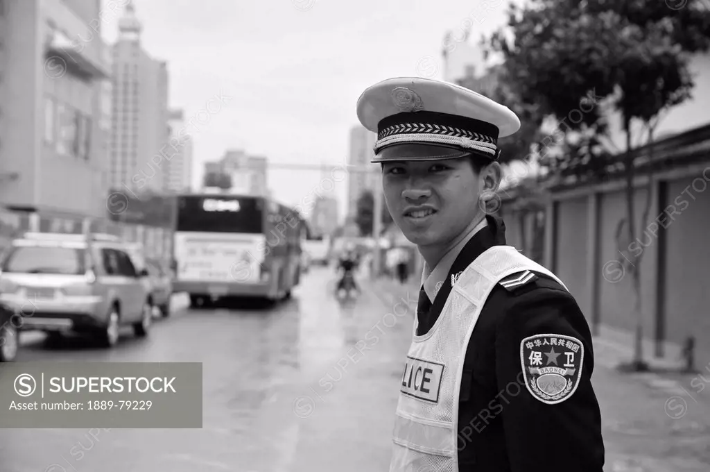 a young policeman standing on the side of a street, ruili yunnan china