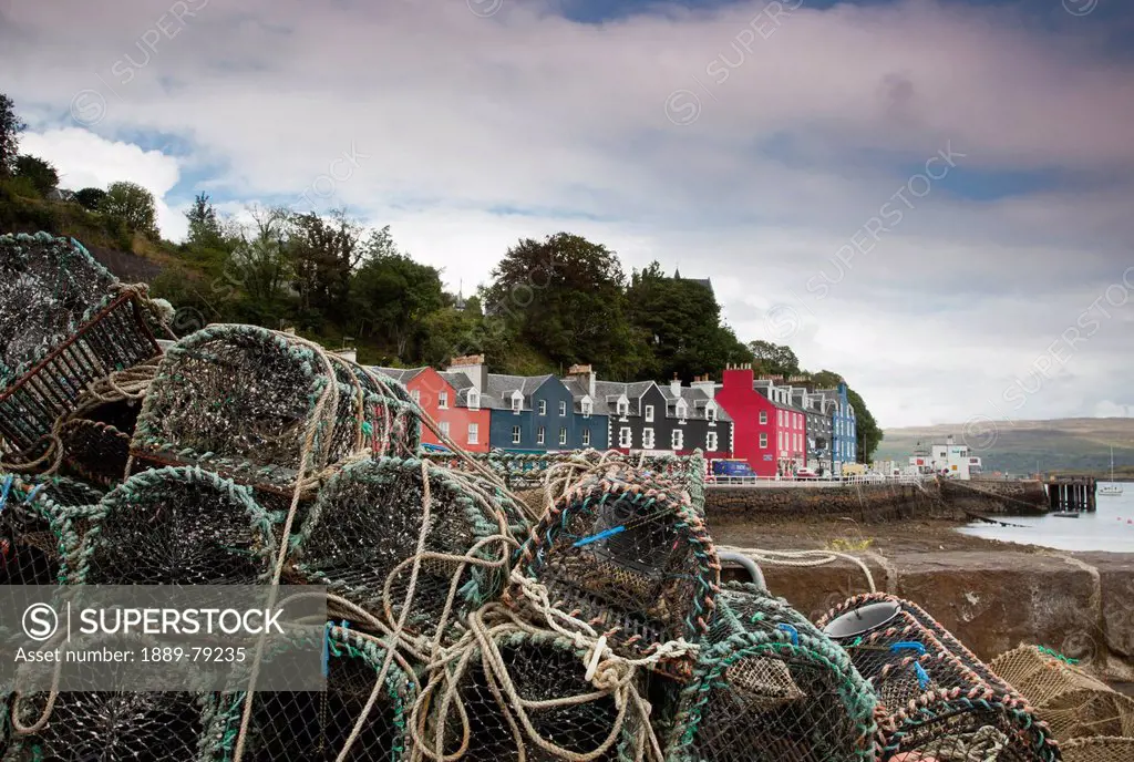 lobster traps on the shore with a row of colourful houses at the water´s edge in the background, tobermory isle of mull scotland