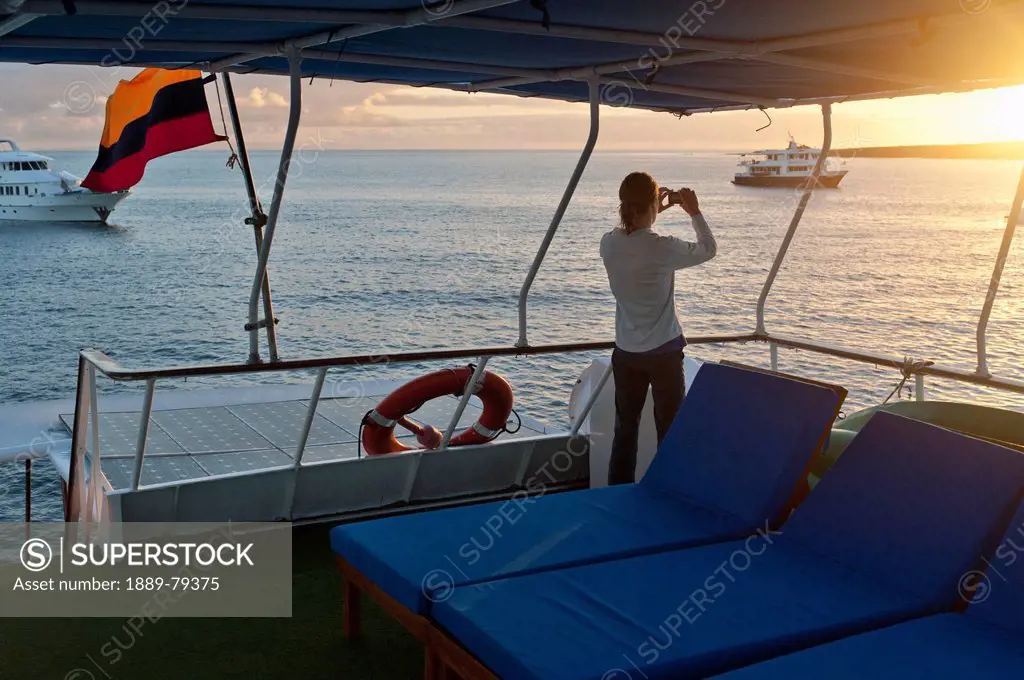 a woman aboard a boat looks out over the water with a camera, punta suarez galapagos equador