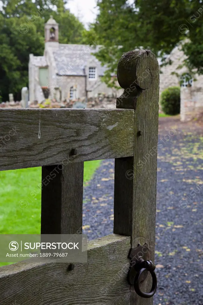 an open gate leading down a path to a cemetery and church, northumberland england