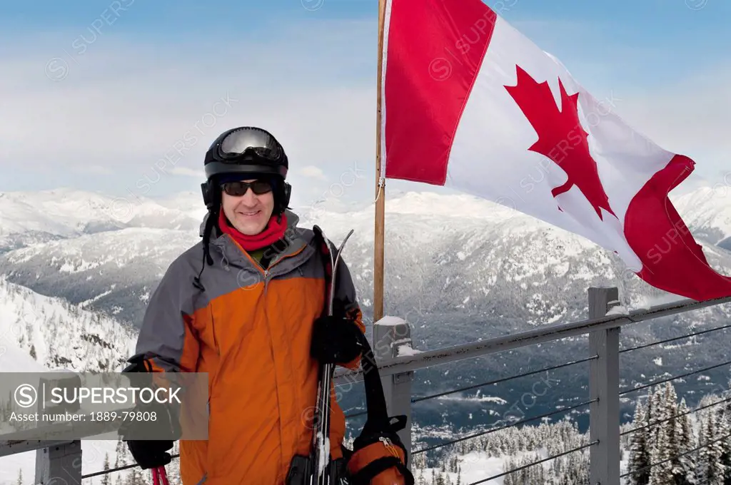 a skier stands beside the canadian flag on a balcony at a ski resort, whistler british columbia canada