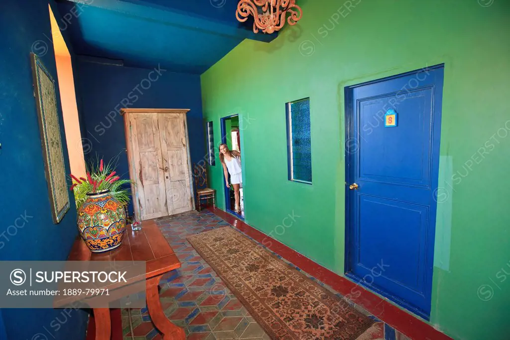 a tourist looks out the door of her room into the hallway of hotel california, todos santos baja california sur mexico
