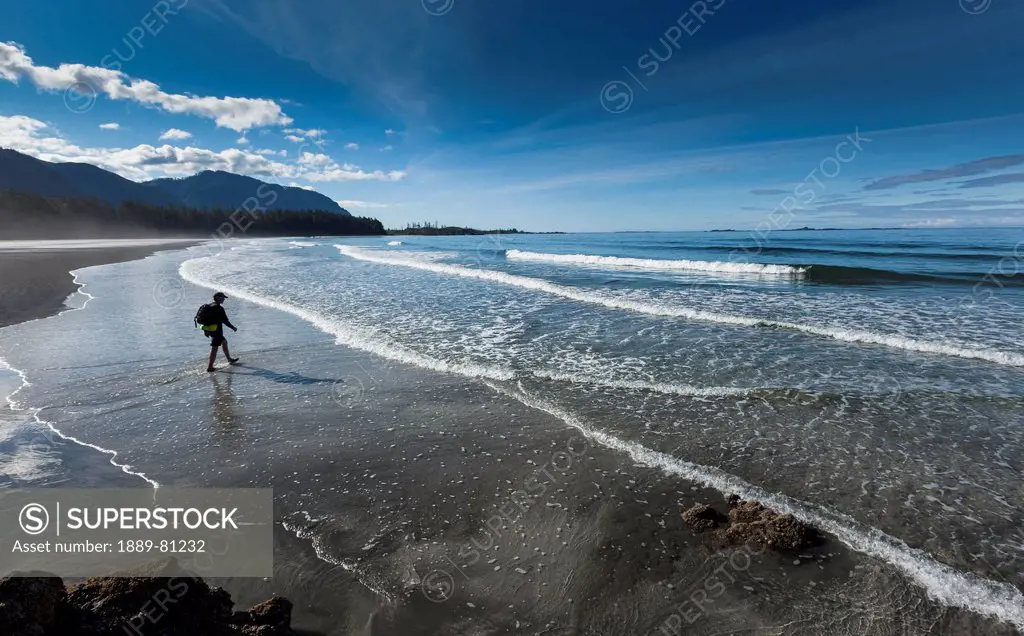 A man walks along the sandy beach of rugged point marine park in a remote area of the west coast of vancouver island, british columbia canada