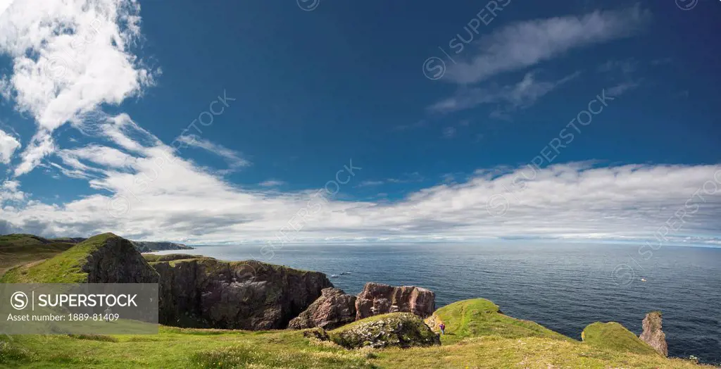 A person stands looking at the rocky promontory at st abb´s head, scottish borders scotland