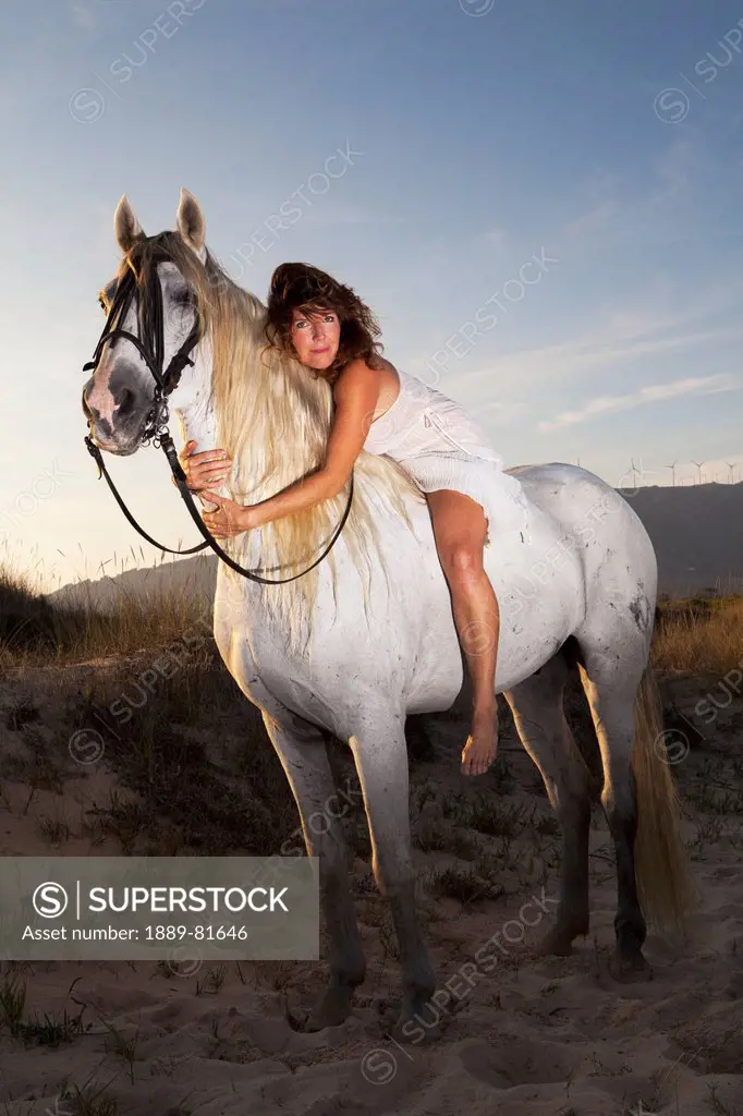 A woman sits bareback on a white horse with her arms embracing the neck of the horse, tarifa cadiz andalusia spain
