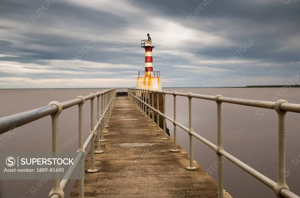 A red and white striped lighthouse at the end of a pier, amble northumberland england