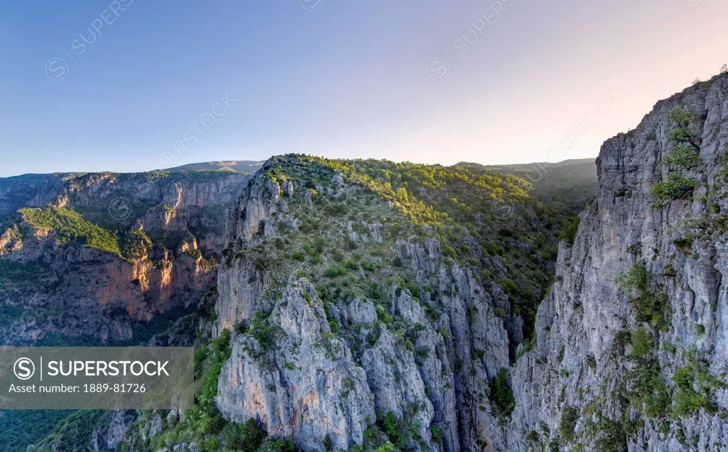 Shafts of light from the early morning sun hit the cliffs and trees on the edge of the vikos gorge at the beloi viewpoint near vradeto, epirus greece