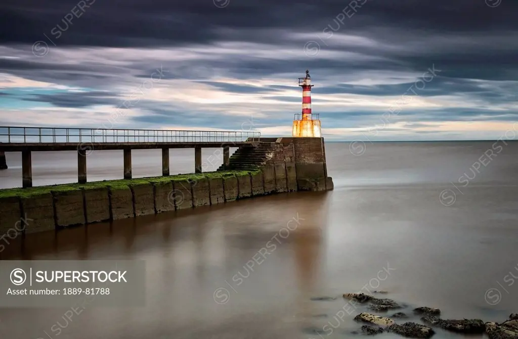 A red and white striped lighthouse at the end of a pier, amble northumberland england