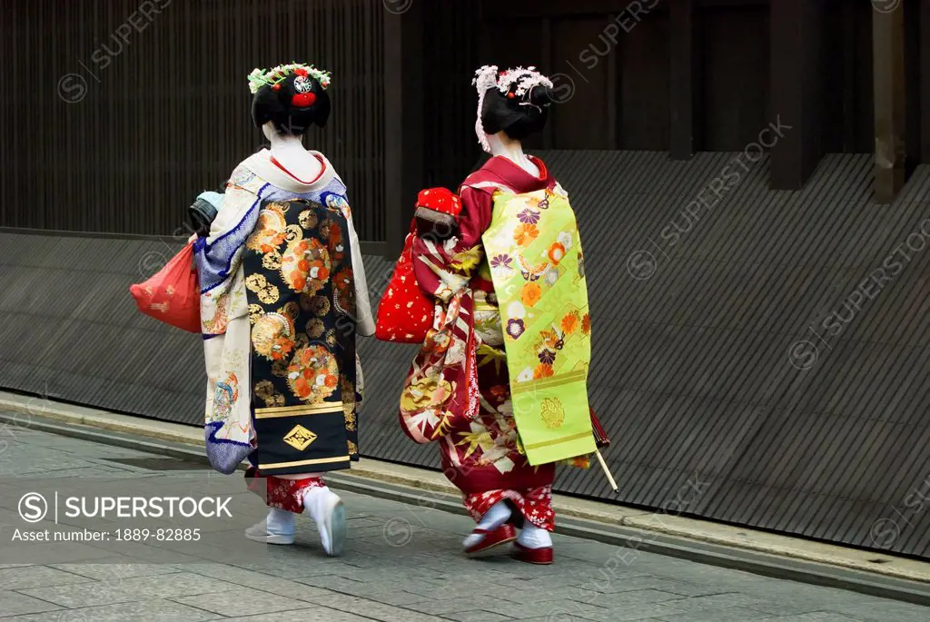 Two maikos apprentice geishas walking away in a street, kyoto, japan
