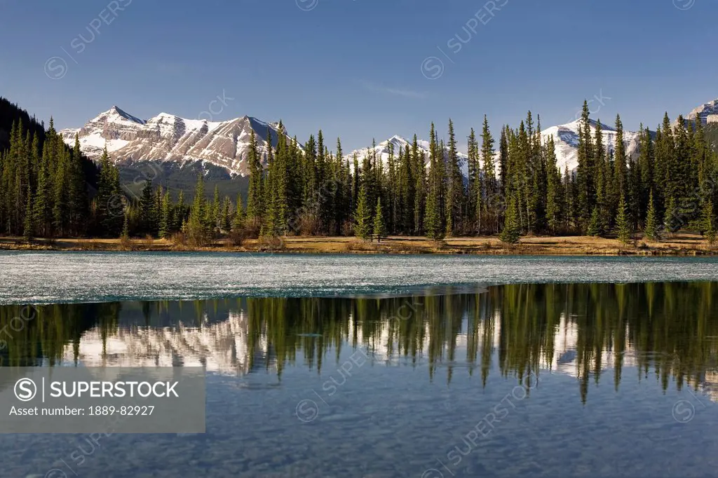 Snow capped mountain range reflecting in a mountain lake with blue sky, alberta, canada
