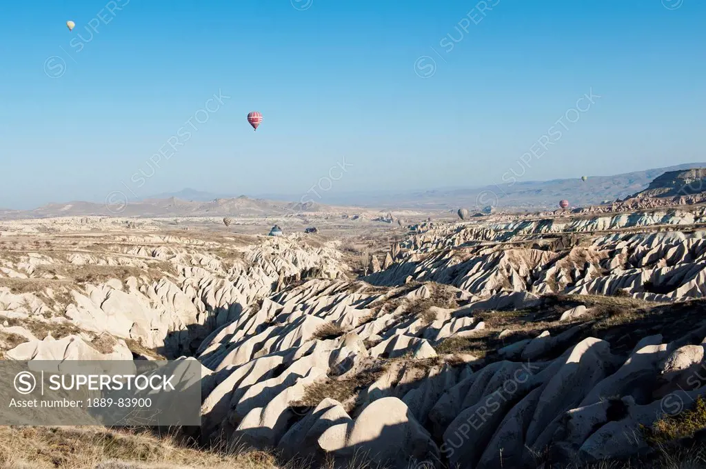 Hot Air Balloons Fill The Blue Sky Over A Rugged Landscape, Nevsehir Turkey