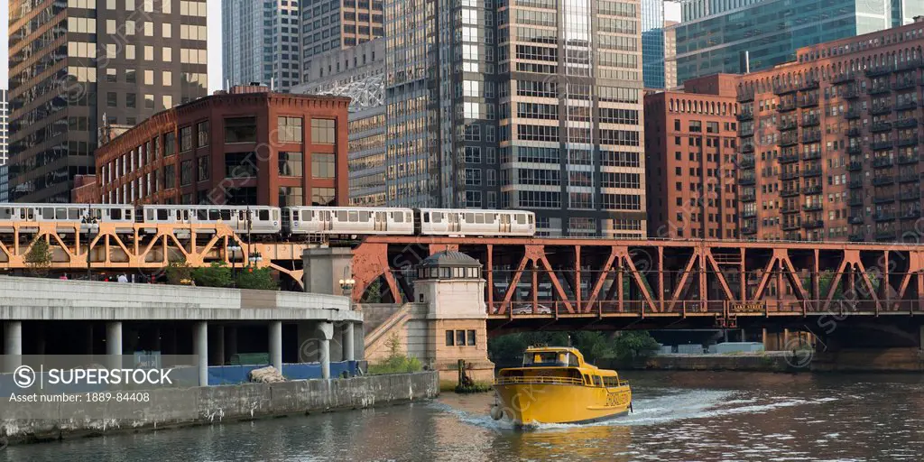 A Yellow Boat In The River Going Under A Bridge With The Train And Buildings In The Background, Chicago Illinois United States Of America