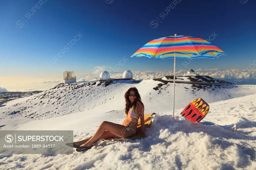 A Woman In Bikini Sitting In The Snow With Beach Umbrella With The View From Mauna Kea Observatories, Mauna Kea Hawaii United States Of America