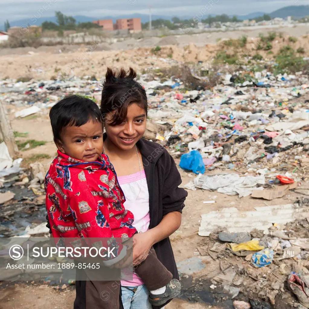 A Girl Holds Her Young Brother While Standing In A Garbage Dump, Guatemala City Guatemala