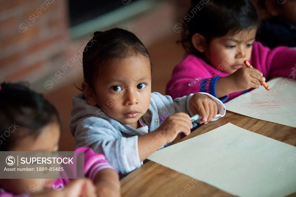 Young Students Sitting At A Table Colouring Paper With Crayons, Guatemala City Guatemala