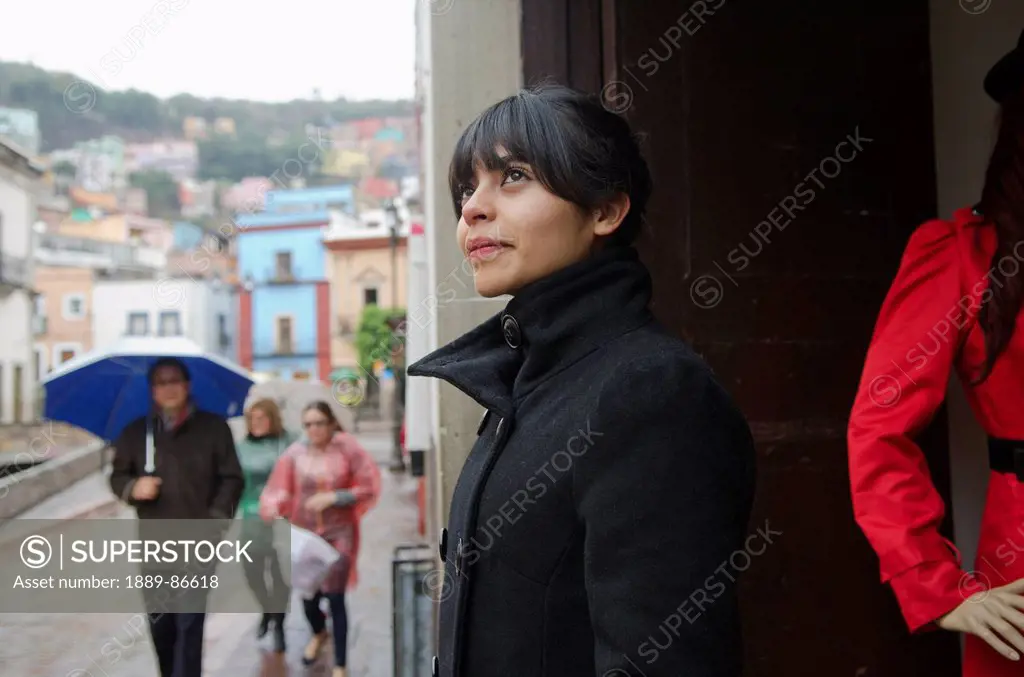 Mexico, Guanajuato, Young Woman Hiding From Rain At Store Display; Guanajuato