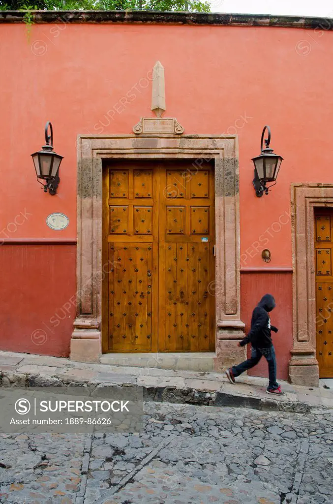 Mexico, Guanajuato, Pedestrian Walking By Old Wooden Door With Large Lanterns; San Miguel De Allende