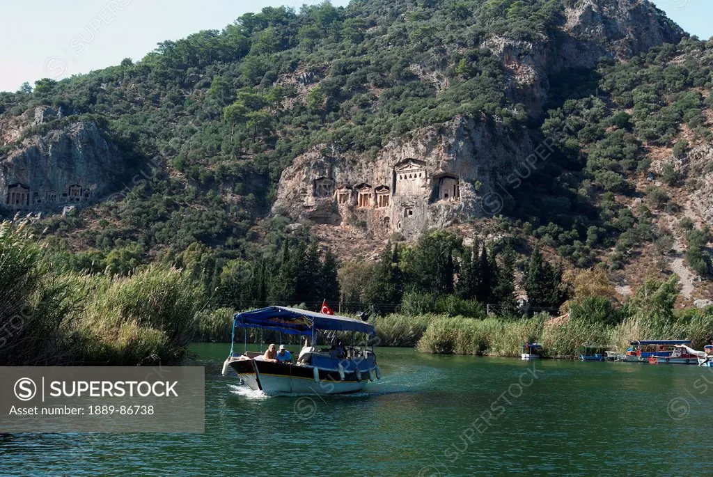 Turkey, Small Tourist Boat Passing Lycian Style Kings Tombs On Dalyan River; Dalyan